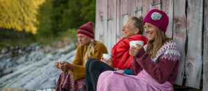 Our three founders sitting by a wooden cabin, enjoying hot beverages and wrapped in blankets.