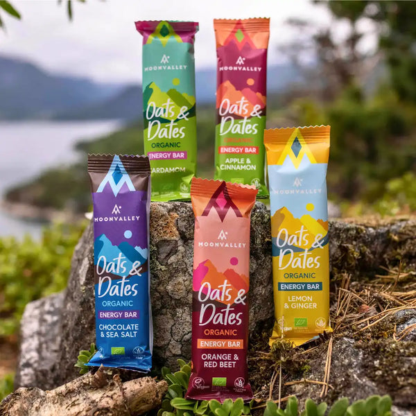 Moonvalleys ekologiska energibars i smakerna kardemumma, äpple och kanel, choklad och havssalt, apelsin och rödbeta samt citron och ingefära i naturskön utomhusmiljö.