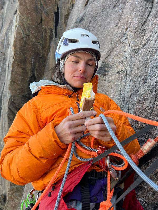 A person wearing a climbing helmet eating a Moonvalley energy bar.