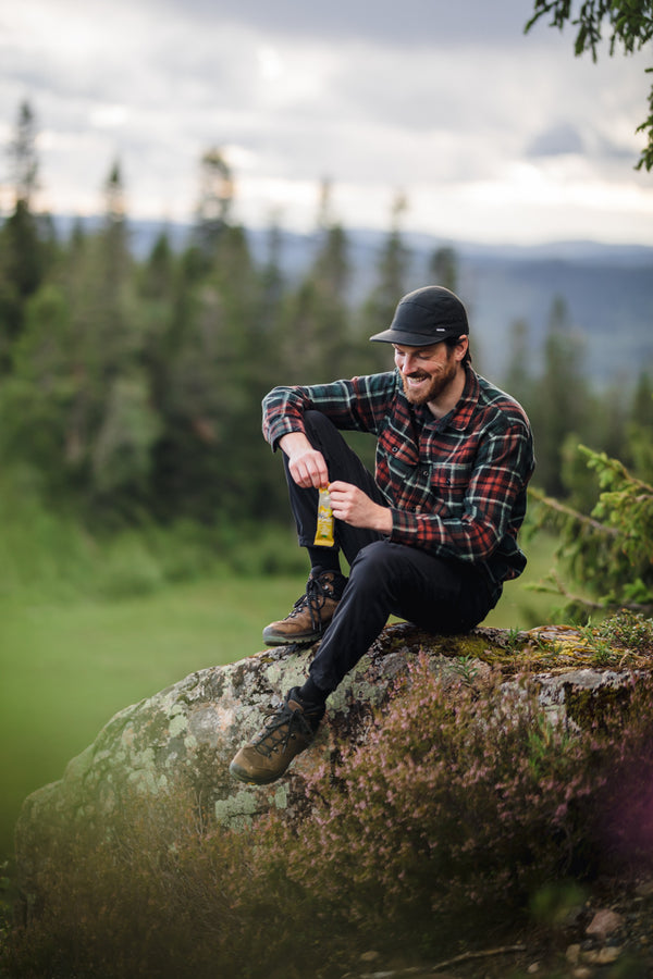 A man sitting on a rock in a forest eating a Moonvalley energy bar.
