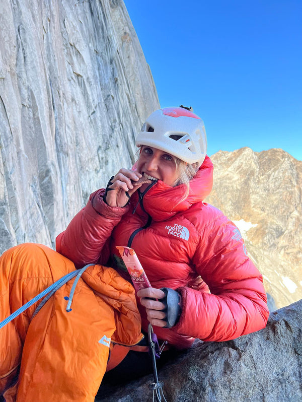 A mountain climber wearing a helmet, eating a Moonvalley energy bar.