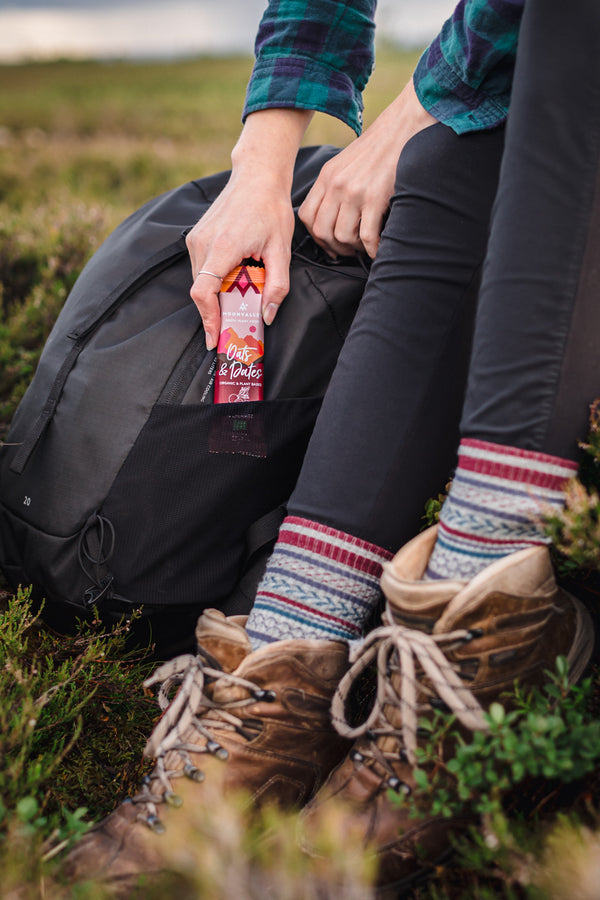 A person sitting with a backpack taking a Moonvalley energy bar out of their side pocket.