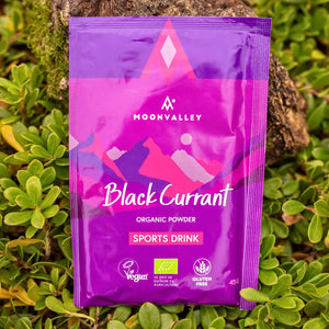 Moonvalley organic Blackcurrant sports drink powder, photographed in a natural outdoor setting.