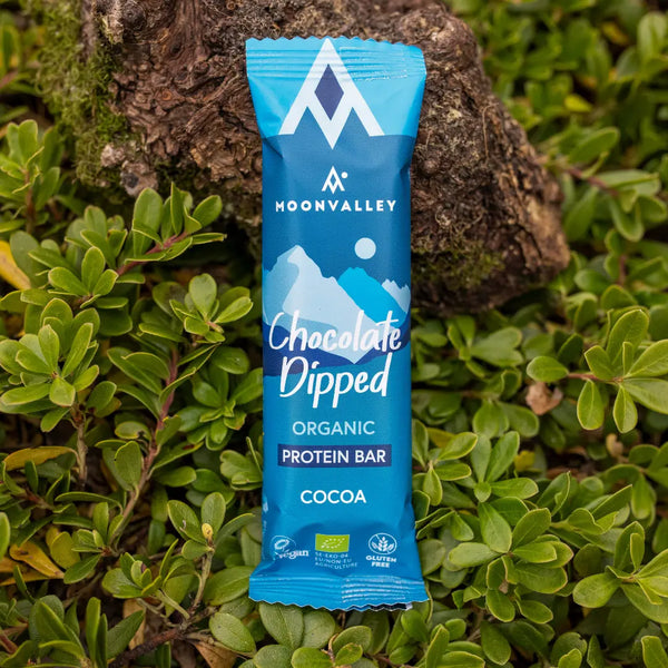 Moonvalley organic cocoa chocolate-coated protein bar, photographed in a natural outdoor setting.