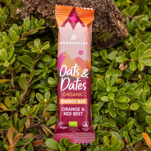 Moonvalley organic Orange & Red Beet energy bar, photographed in a natural outdoor setting.