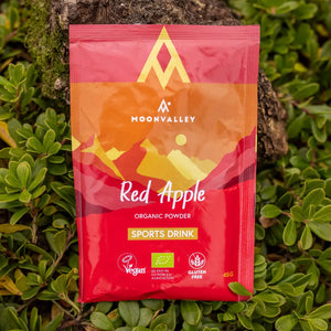 Moonvalley organic Red Apple sports drink powder, photographed in a natural outdoor setting.