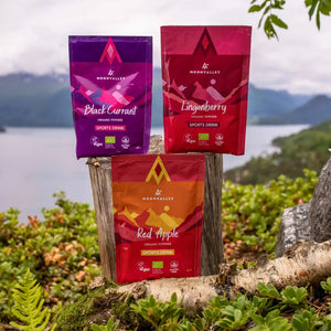 Moonvalley organic sports drink powders in Blackcurrant, Lingonberry and Red Apple flavours displayed in a scenic outdoor setting.
