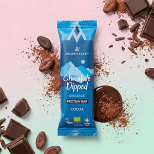 Organic Chocolate-Dipped Cocoa protein bar surrounded by dark chocolate chunks and cocoa powder.