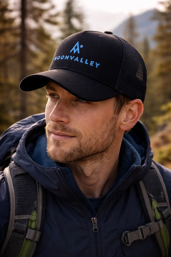Man wearing a black cap with 'MoonyValley' logo and a backpack in a forest setting