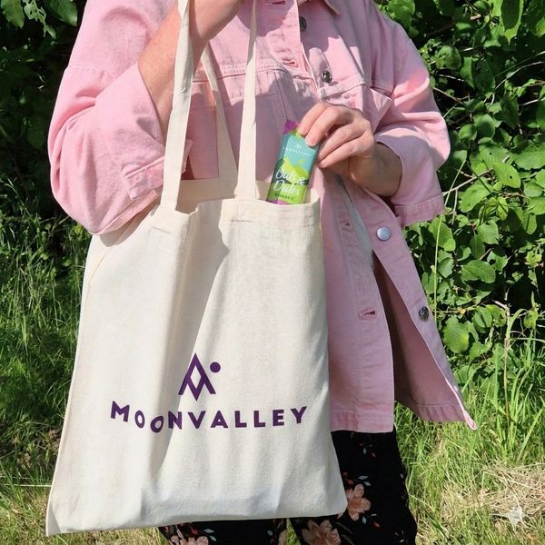 Close-up of the Moonvalley tote bag showing the purple logo design and a protein bar.
