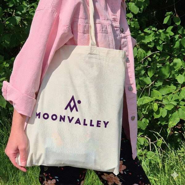 Person carrying a Moonvalley cotton tote bag with a purple logo.