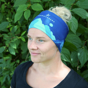 Woman wearing a blue Moonvalley Mountain Tube as a headband in a forest setting.